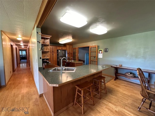 kitchen with brown cabinets, a sink, light wood-style flooring, a peninsula, and fridge with ice dispenser