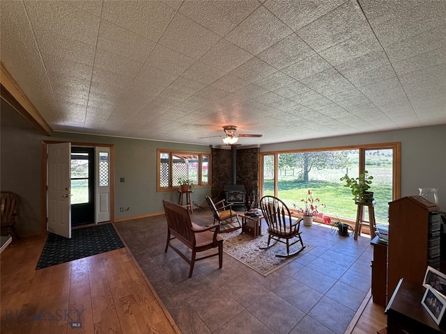 living room featuring a wood stove, ceiling fan, a wealth of natural light, and wood-type flooring