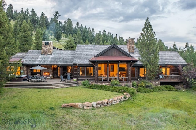 back of property featuring a wooden deck, a fireplace, and a lawn