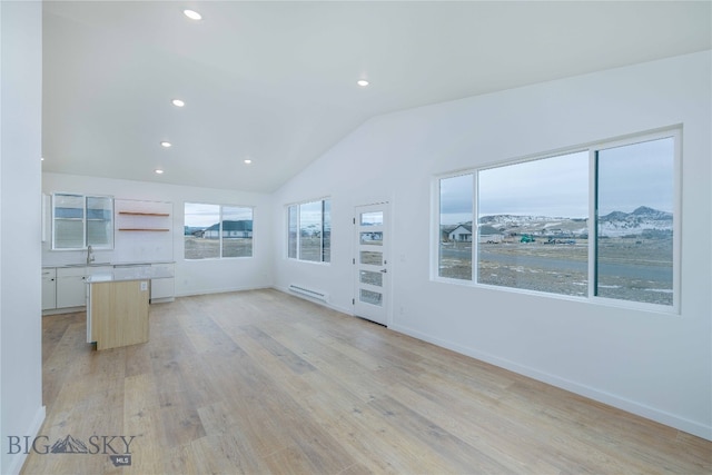 empty room featuring a mountain view, light hardwood / wood-style floors, baseboard heating, sink, and lofted ceiling