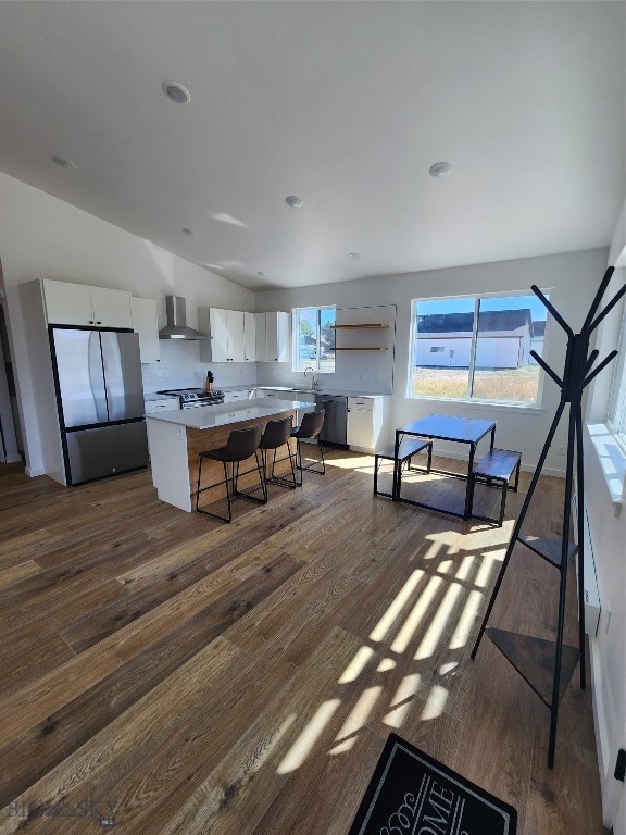 kitchen with wood-type flooring, wall chimney range hood, a breakfast bar, white cabinets, and appliances with stainless steel finishes