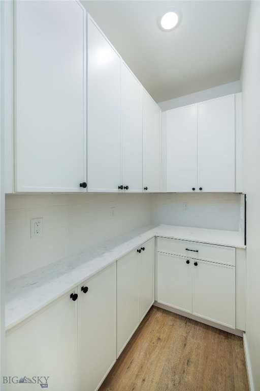 kitchen featuring white cabinets, light hardwood / wood-style floors, light stone countertops, and tasteful backsplash