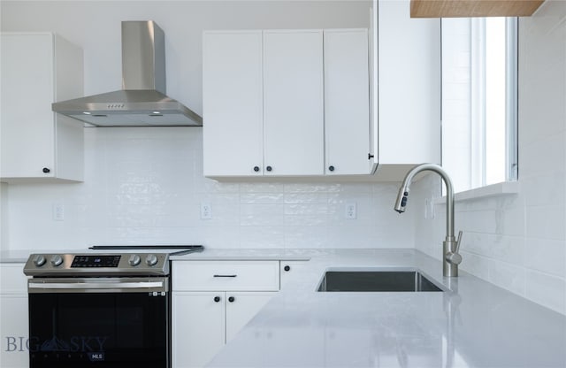 kitchen with stainless steel electric range, backsplash, wall chimney range hood, sink, and white cabinets