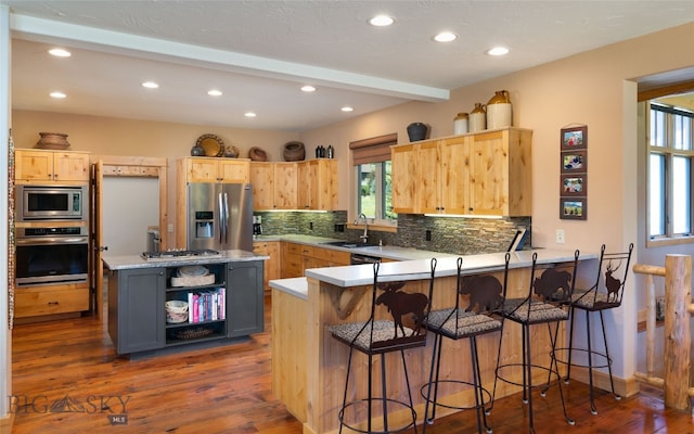 kitchen featuring appliances with stainless steel finishes, a breakfast bar area, tasteful backsplash, kitchen peninsula, and dark hardwood / wood-style flooring