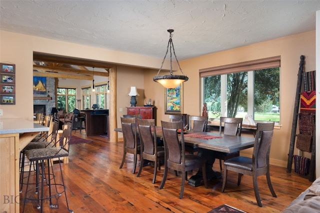 dining room featuring a textured ceiling, a fireplace, dark hardwood / wood-style floors, and beam ceiling