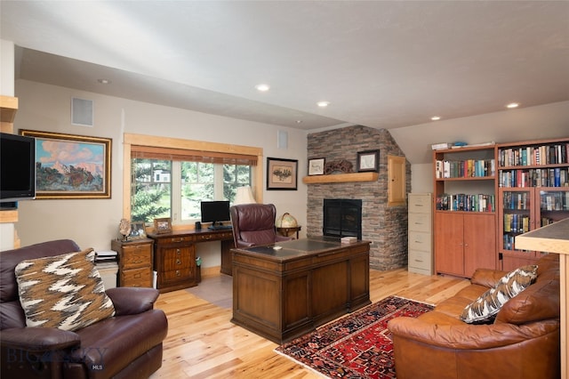 office area with vaulted ceiling, a stone fireplace, and light wood-type flooring