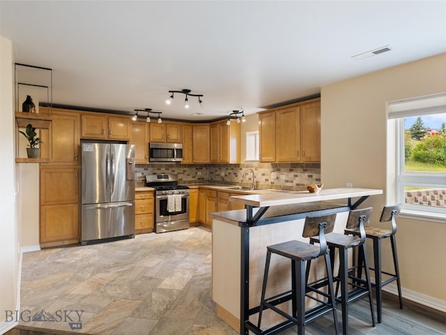 kitchen with kitchen peninsula, stainless steel appliances, backsplash, a breakfast bar area, and sink