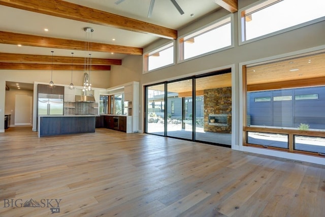 unfurnished living room with beamed ceiling, ceiling fan, light hardwood / wood-style flooring, and a high ceiling