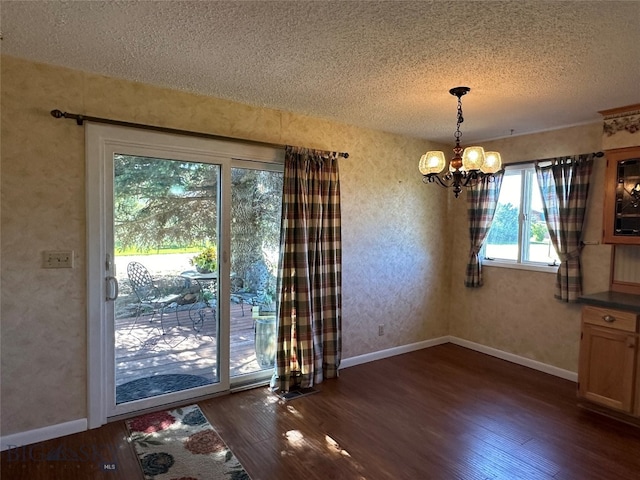 unfurnished dining area featuring a textured ceiling, dark hardwood / wood-style floors, and an inviting chandelier