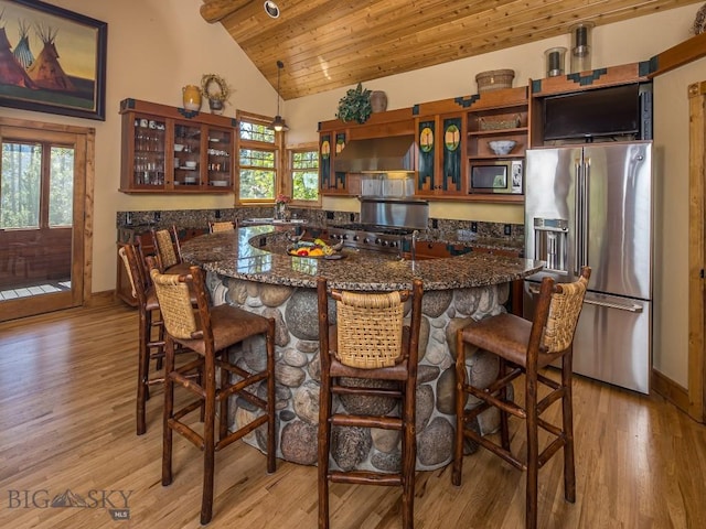 kitchen with wood ceiling, plenty of natural light, appliances with stainless steel finishes, a kitchen breakfast bar, and wall chimney range hood