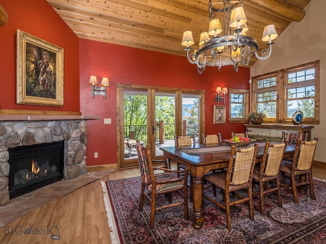 dining area featuring hardwood / wood-style flooring, a stone fireplace, vaulted ceiling, wooden ceiling, and a chandelier