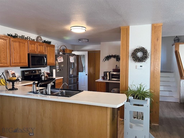 kitchen with kitchen peninsula, wood-type flooring, appliances with stainless steel finishes, sink, and a textured ceiling