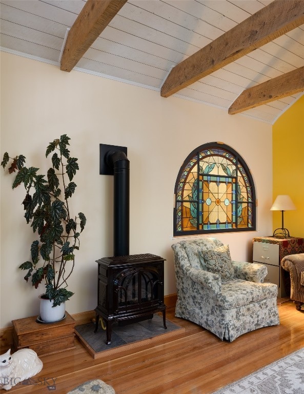 sitting room featuring a wood stove, hardwood / wood-style flooring, and beamed ceiling