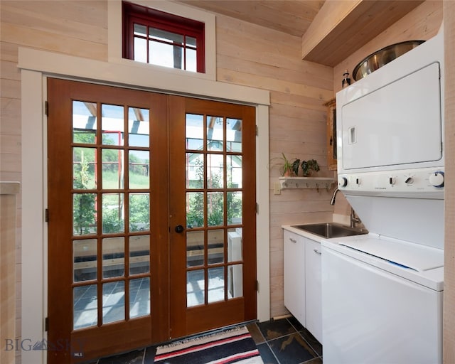 washroom with french doors, stacked washer / dryer, cabinets, and wooden walls