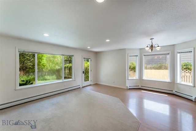 unfurnished room featuring a notable chandelier, baseboard heating, a healthy amount of sunlight, and hardwood / wood-style floors