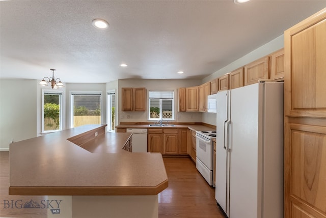 kitchen featuring hardwood / wood-style flooring, hanging light fixtures, white appliances, an inviting chandelier, and a kitchen island