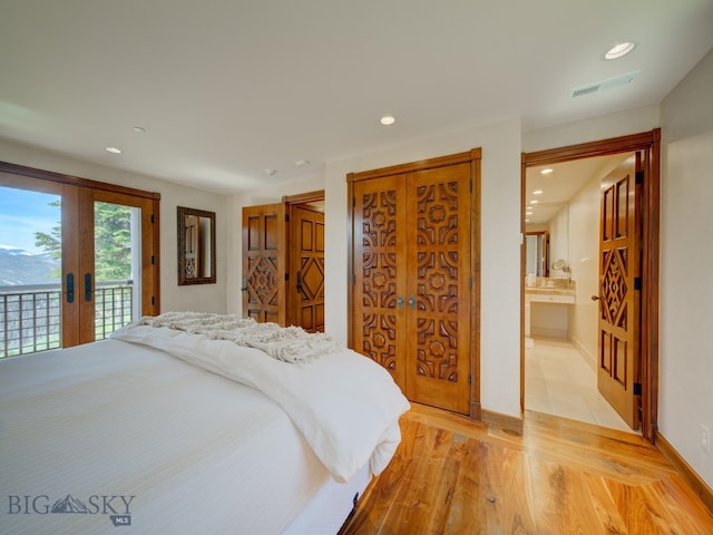 bedroom with light hardwood / wood-style floors, ensuite bath, french doors, and access to exterior