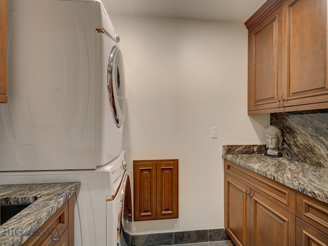 laundry area with stacked washer / dryer, dark tile patterned flooring, and cabinets