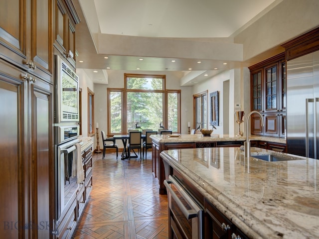 kitchen with light stone countertops, parquet flooring, sink, and built in appliances