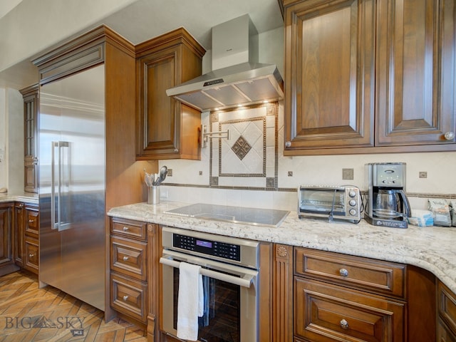 kitchen featuring wall chimney range hood, light parquet floors, appliances with stainless steel finishes, and light stone counters