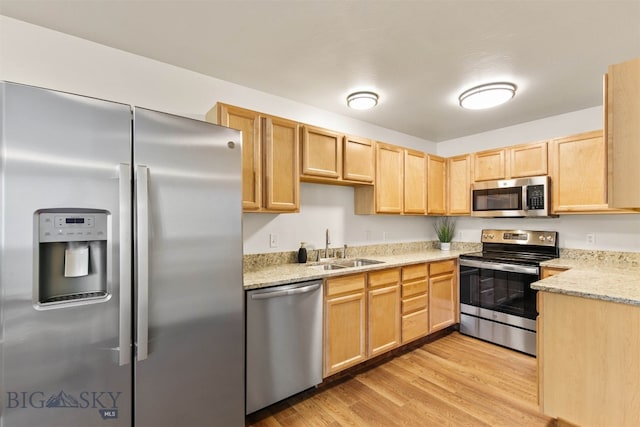 kitchen featuring appliances with stainless steel finishes, sink, light stone counters, light hardwood / wood-style floors, and light brown cabinets