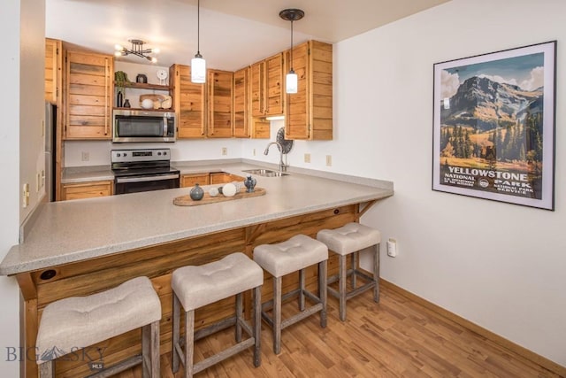 kitchen featuring light wood-type flooring, kitchen peninsula, stainless steel appliances, and hanging light fixtures