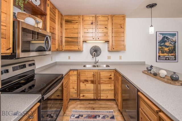 kitchen featuring light wood-style flooring, stainless steel appliances, light countertops, pendant lighting, and a sink