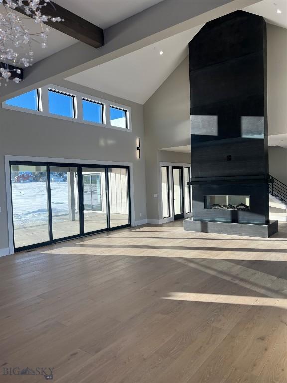 unfurnished living room featuring beamed ceiling, a towering ceiling, an inviting chandelier, and hardwood / wood-style flooring