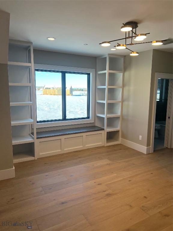 unfurnished living room featuring an inviting chandelier and light hardwood / wood-style flooring