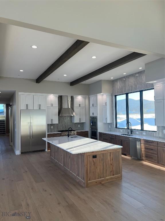 kitchen featuring white cabinetry, appliances with stainless steel finishes, wall chimney exhaust hood, and a large island