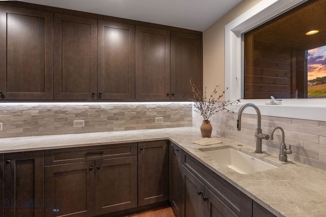 kitchen with dark brown cabinets, light wood-type flooring, tasteful backsplash, light stone counters, and sink