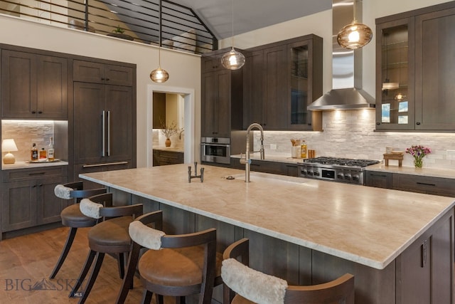 kitchen featuring hanging light fixtures, decorative backsplash, hardwood / wood-style floors, wall chimney exhaust hood, and a kitchen island with sink