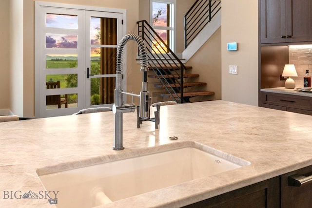 room details featuring sink, dark brown cabinets, tasteful backsplash, and light stone counters