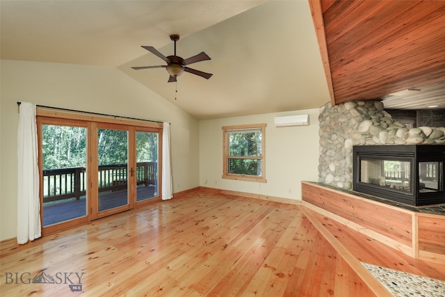 unfurnished living room featuring lofted ceiling, a wall mounted air conditioner, hardwood / wood-style flooring, ceiling fan, and a fireplace