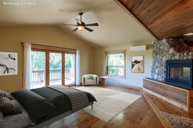 bedroom featuring multiple windows, an AC wall unit, access to outside, and a stone fireplace