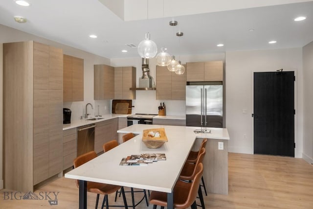 kitchen featuring sink, wall chimney exhaust hood, light hardwood / wood-style flooring, an island with sink, and appliances with stainless steel finishes