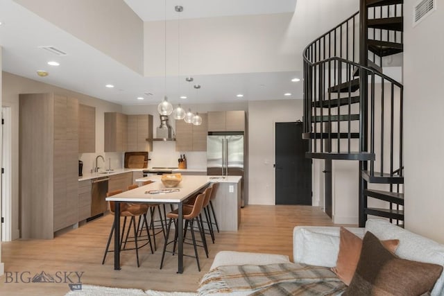 kitchen featuring a center island, wall chimney range hood, hanging light fixtures, light hardwood / wood-style floors, and stainless steel appliances