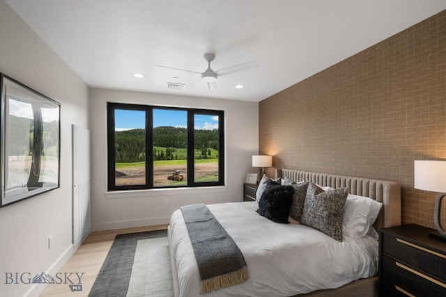 bedroom featuring ceiling fan, light hardwood / wood-style flooring, and tile walls