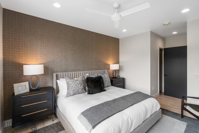 bedroom featuring ceiling fan, light wood-type flooring, and tile walls