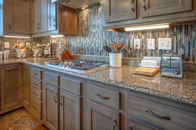 kitchen with wall chimney exhaust hood, stone countertops, stainless steel gas cooktop, and backsplash