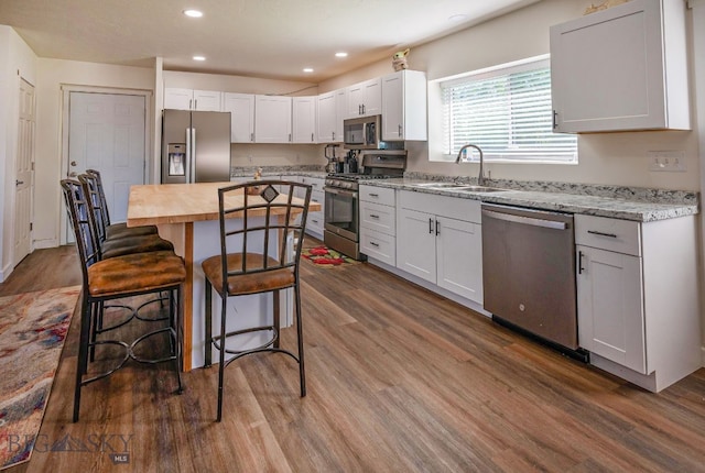 kitchen featuring hardwood / wood-style floors, white cabinetry, sink, light stone counters, and stainless steel appliances