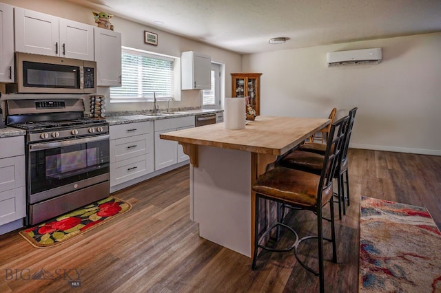 kitchen with a breakfast bar, appliances with stainless steel finishes, a wall mounted AC, white cabinets, and wood counters