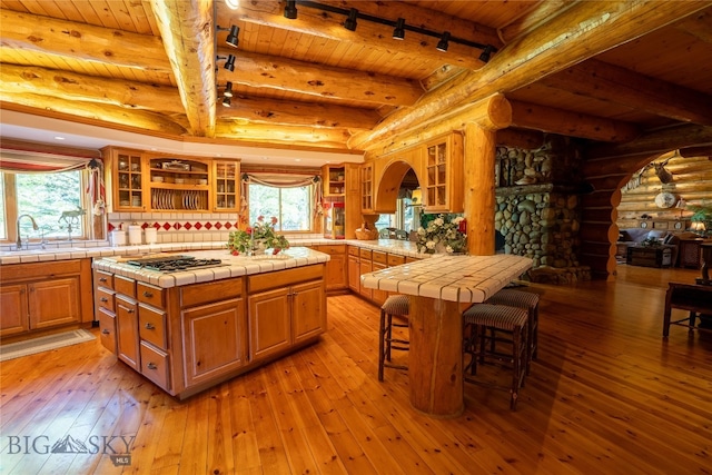 kitchen with log walls, light wood-type flooring, tile counters, and a wealth of natural light