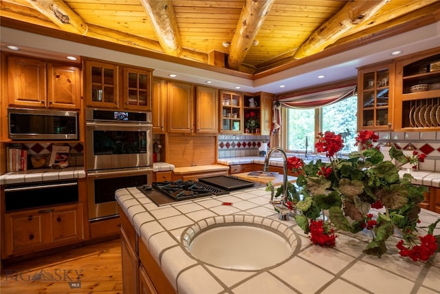 kitchen with stainless steel appliances, tile counters, light hardwood / wood-style floors, and wood ceiling