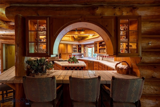 bar featuring dishwashing machine, tile counters, and log walls