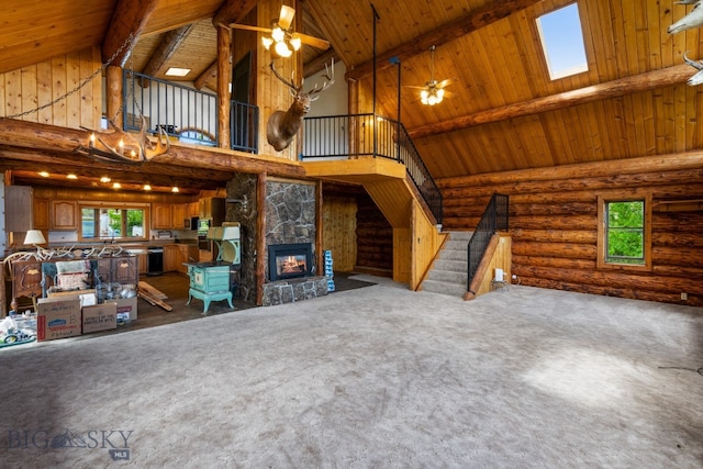 unfurnished living room with a skylight, wood ceiling, log walls, ceiling fan, and a stone fireplace