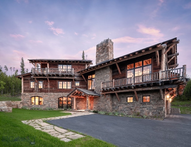 back house at dusk featuring a balcony and a lawn