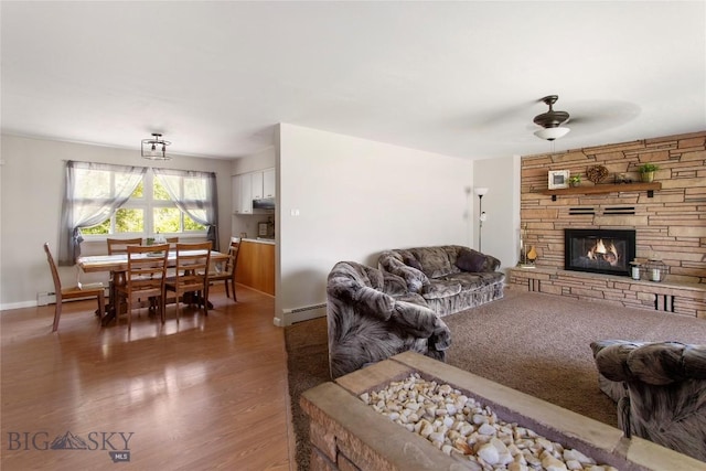 living room featuring baseboards, ceiling fan, dark wood-style flooring, a stone fireplace, and a baseboard heating unit