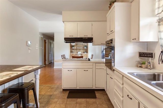 kitchen with oven, under cabinet range hood, a peninsula, white cabinets, and light countertops