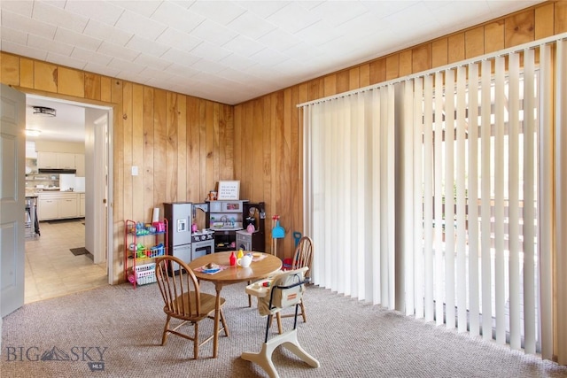 dining room featuring wooden walls and light colored carpet